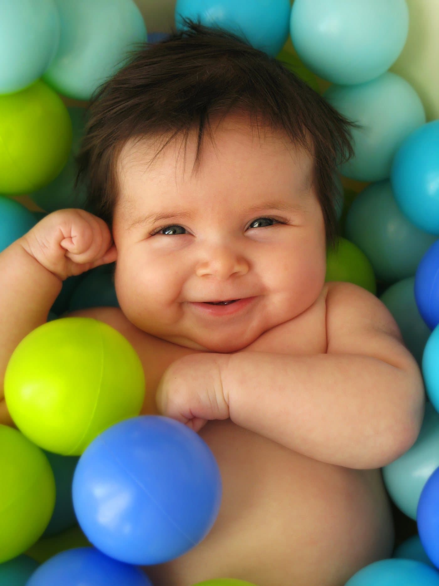 A smiling baby lying among colorful balls